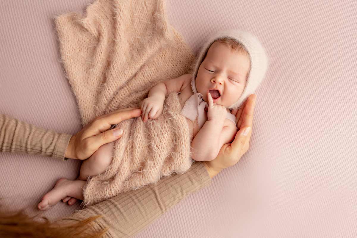 Suesses-Baby-in-den-Armen-der-Mutter-waehrend-einer-Neugeborenen-Fotosesion